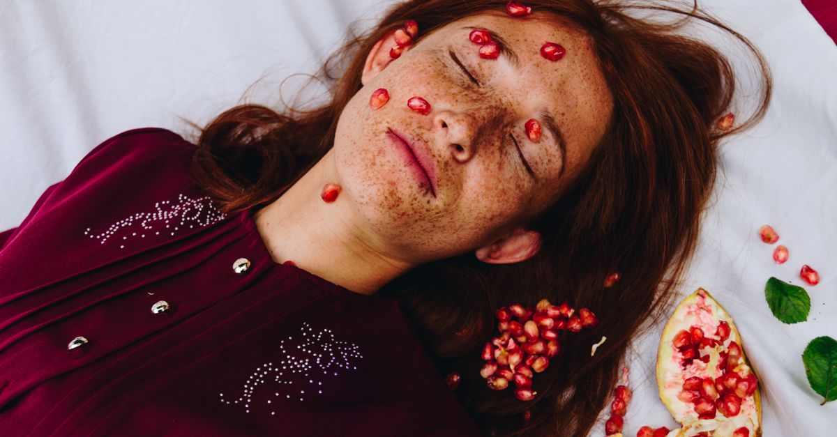 From above of young calm female with long red hair and freckles lying on comfortable bed with closed eyes and pomegranate grains on face - Evidence evidence guide for pomegranate eye fatigue randomized trial