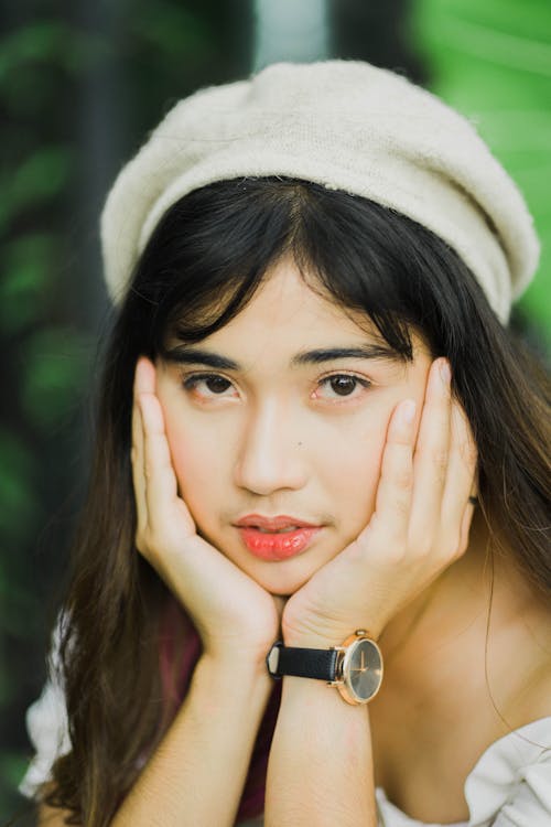 Free Serene young Asian female in stylish beret touching face with hands in lush park and looking at camera Stock Photo