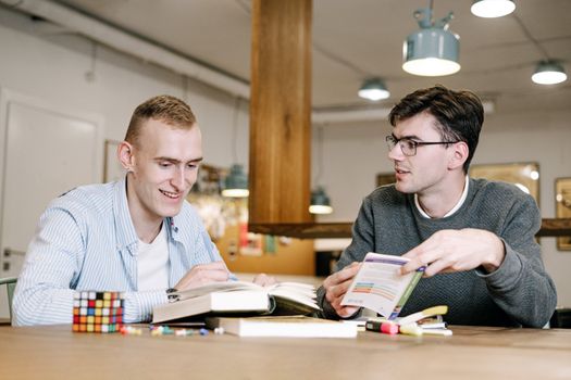 两个年轻人在桌旁一起学习，在室内阅读书籍和笔记