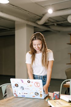 Cheerful woman using a laptop with stickers in a modern indoor office setting.