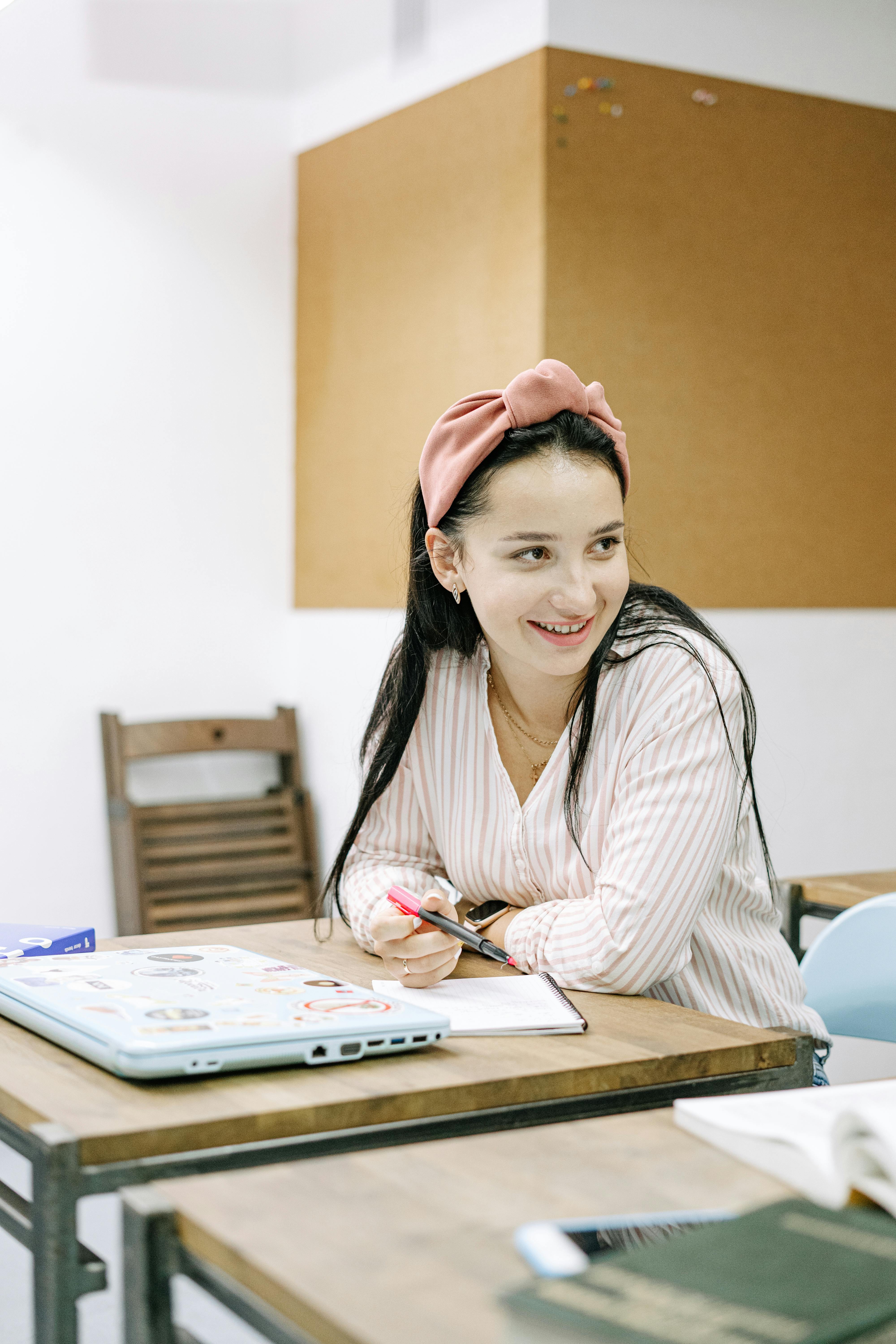 一名戴着粉色头带的年轻女子在室内办公桌前微笑着学习