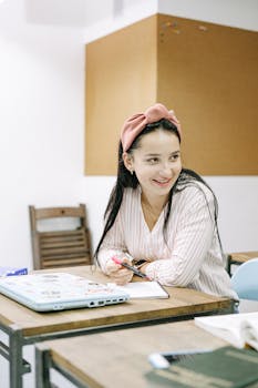 一名戴着粉色头带的年轻女子在室内办公桌前微笑着学习