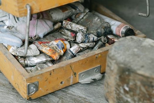 A worn wooden box filled with used paint tubes and art supplies, exuding a vintage vibe.