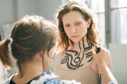 Free An artist applies intricate body paint on a thoughtful model. Creative expressions in studio lighting. Stock Photo