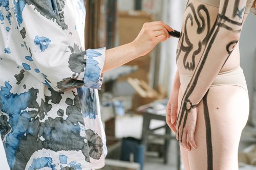 Free Close-up of an artist painting a model's body with creative designs in a studio. Stock Photo