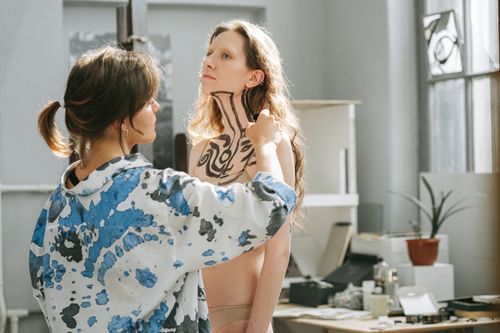 Free An artist paints intricate patterns on a woman's body in a well-lit art studio. Stock Photo