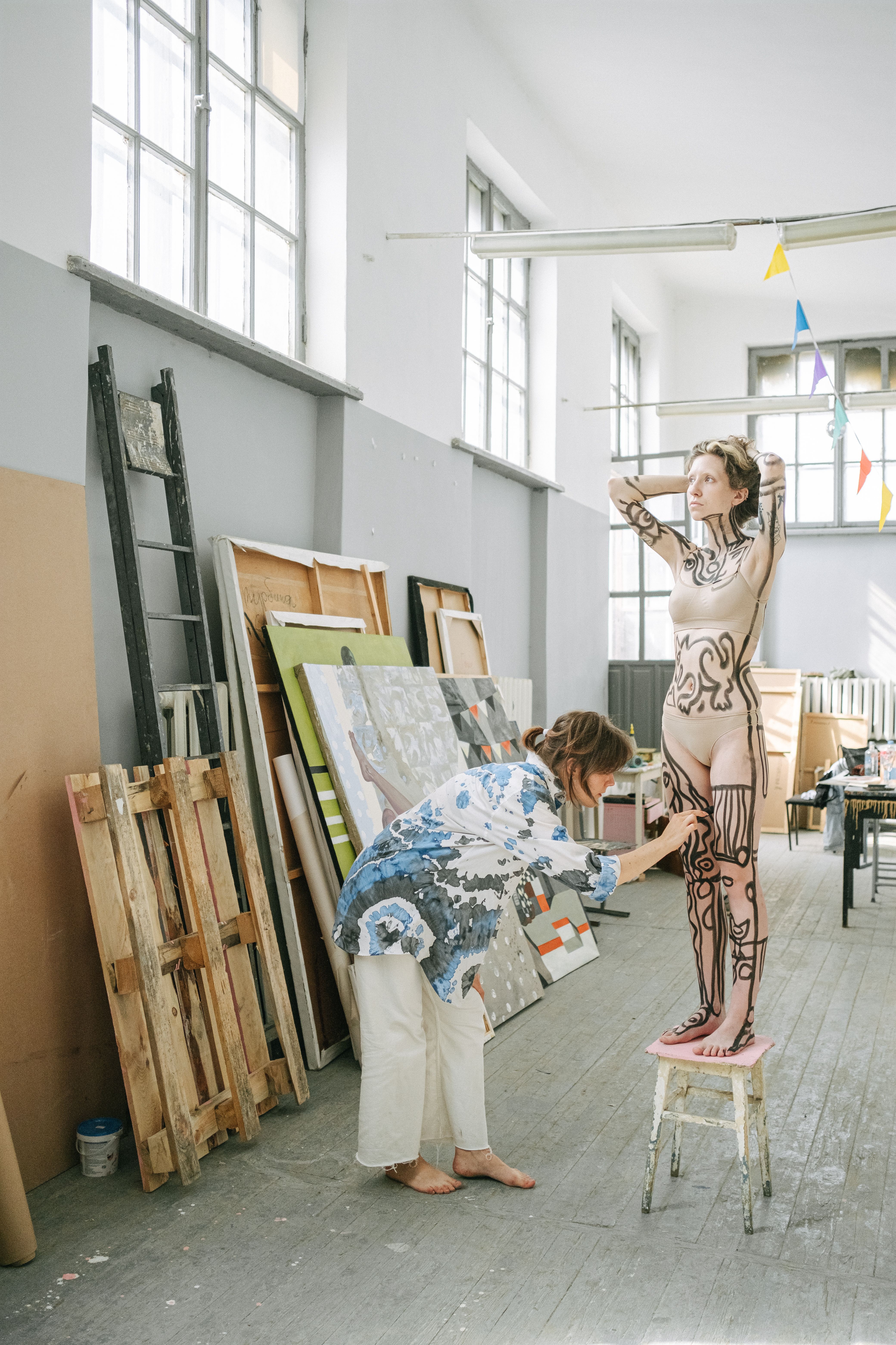 Artist painting body art on a model in a spacious studio.