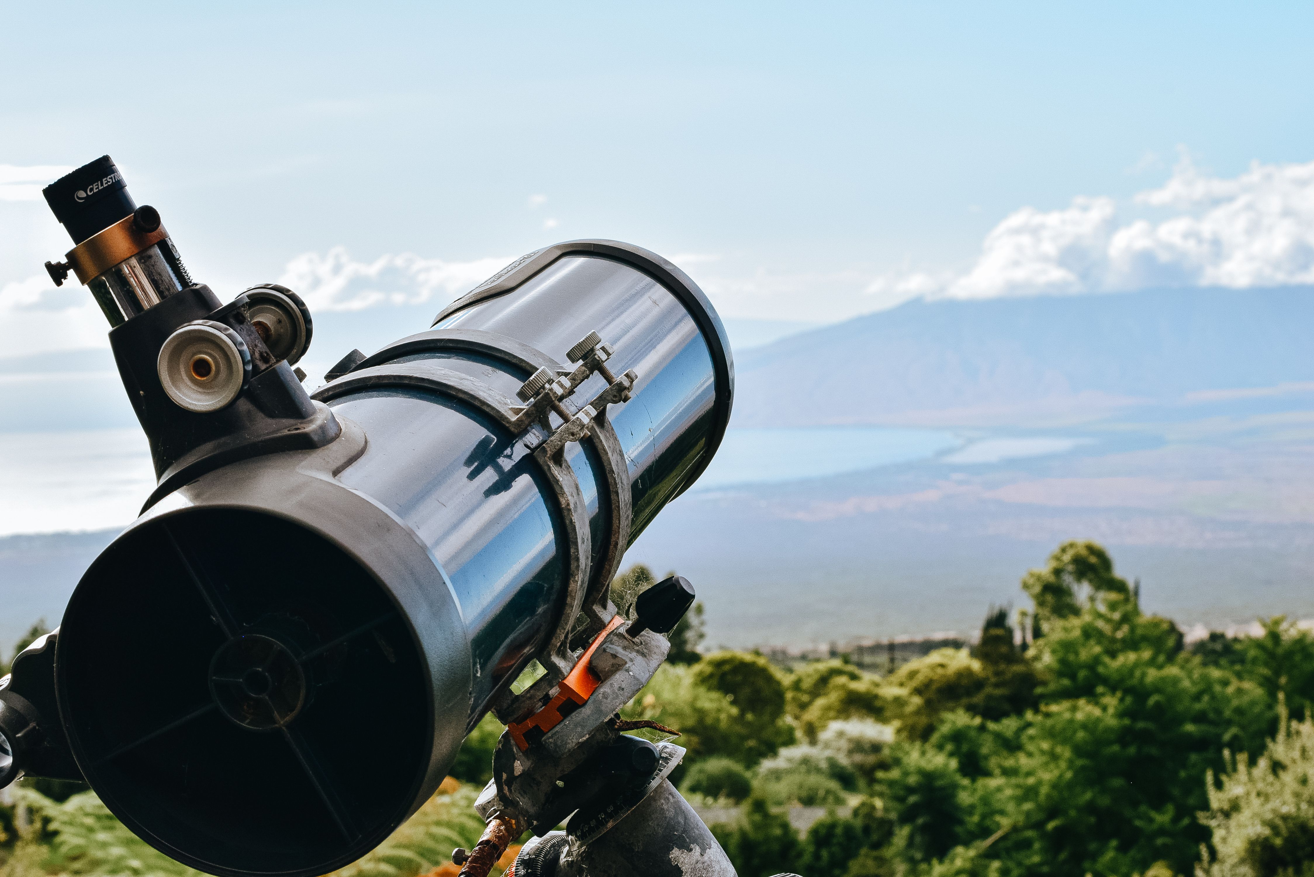 Blue calm ocean near mountains and lush forest behind telescope on hill in summer