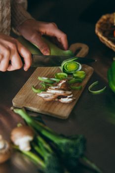 Close-up view of a person slicing vegetables on a wooden chopping board in a kitchen setting.