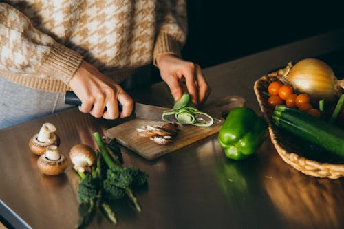 Person Slicing a Vegetable on Wooden Chopping Board