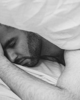A serene black and white image of a young man sleeping peacefully under a blanket.