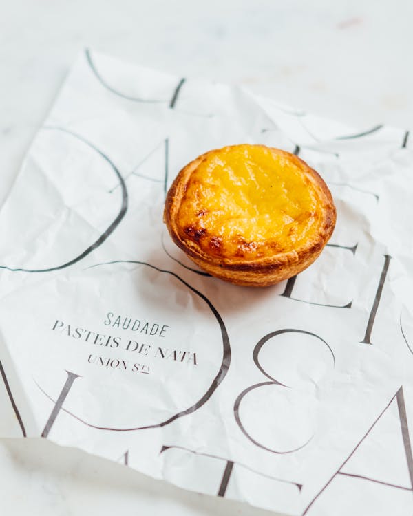 Small appetizing round yellow Portuguese eggs tart on paper tissue with inscription on surface in bright room