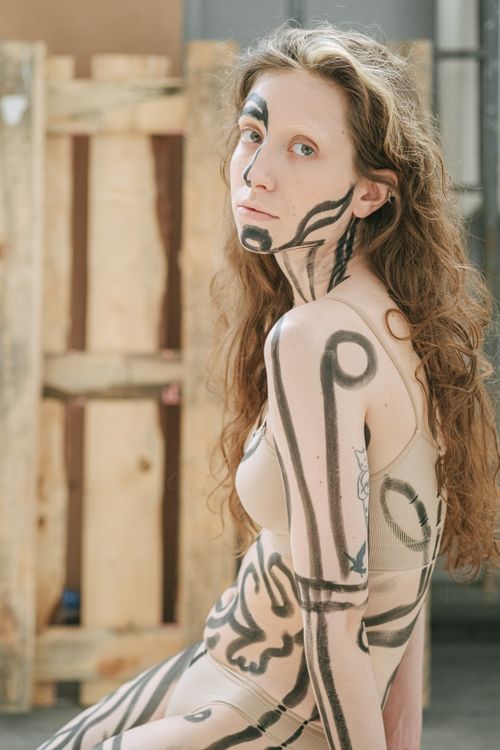 Free Caucasian woman covered in abstract body paint, posing in an artistic studio setting. Stock Photo