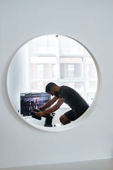 Focused man on a stationary bike in a bright home setting, captured through a round mirror.