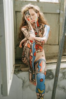 一位白人妇女坐在乡村房间里，身上色彩缤纷的人体艺术表达出沉思
