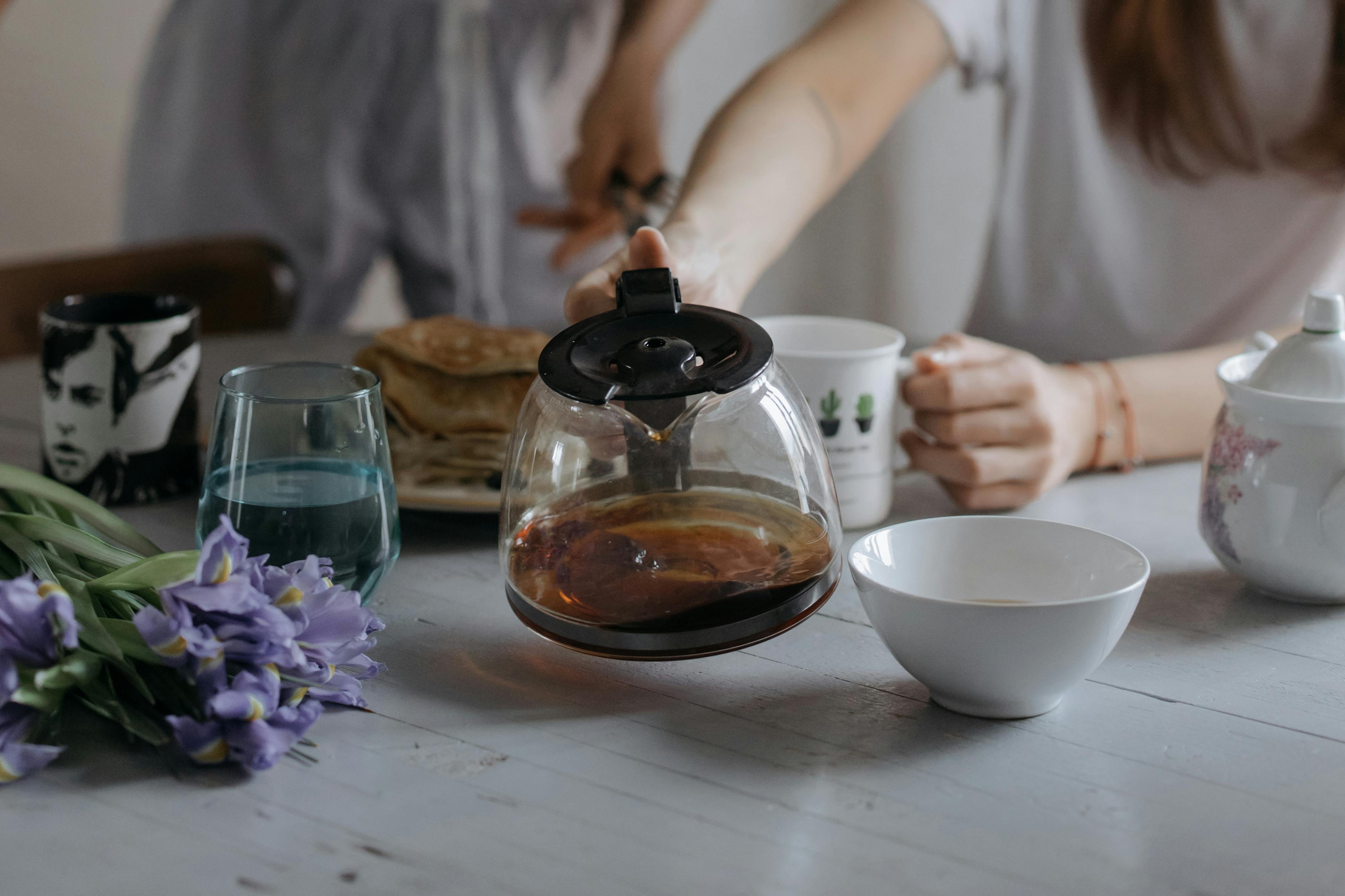A serene morning breakfast scene featuring a coffee pot, pancakes, and flowers on a table.