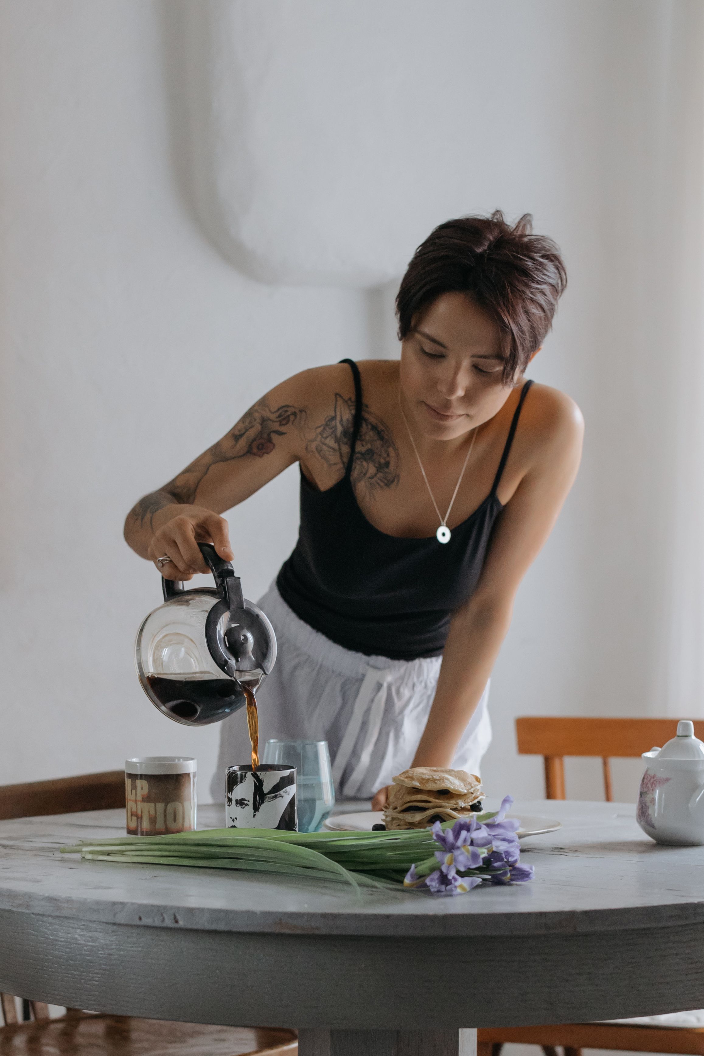 一名年轻女子将咖啡、煎饼和虹膜摆在桌上，营造出极简主义的早餐场景