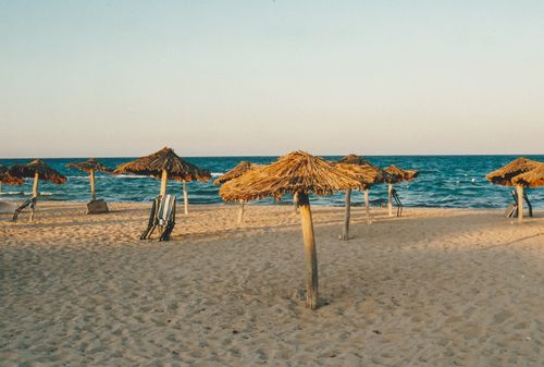 Free A tranquil sandy beach with straw umbrellas by the ocean under clear skies. Stock Photo