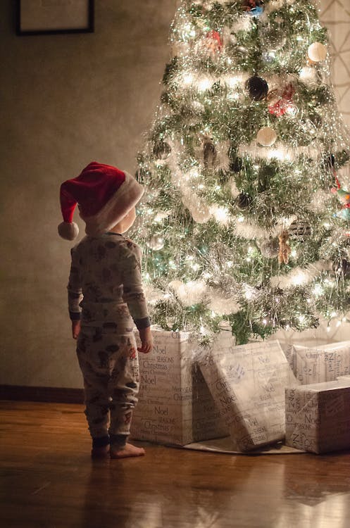 Photo of a Kid Standing Near a Christmas Tree