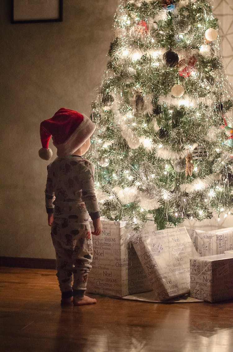 Photo Of A Kid Standing Near A Christmas Tree