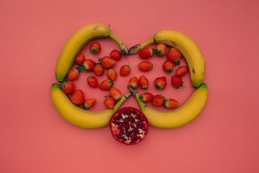 A vibrant display of bananas, strawberries, and pomegranate on a pink background.