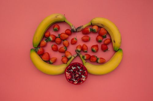 Free A vibrant display of bananas, strawberries, and pomegranate on a pink background. Stock Photo