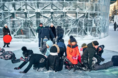 Free Group of children enjoying a snowy day playing on an ice sculpture in a winter park with warm clothing. Stock Photo