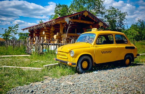 Free Yellow Taxi Cab Parked Beside a Wooden House Stock Photo