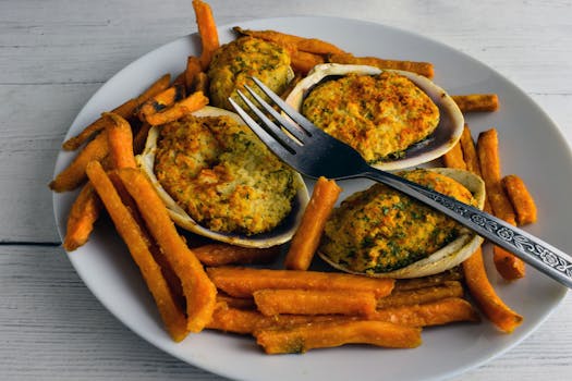Tasty stuffed clams paired with crispy sweet potato fries on a white plate.