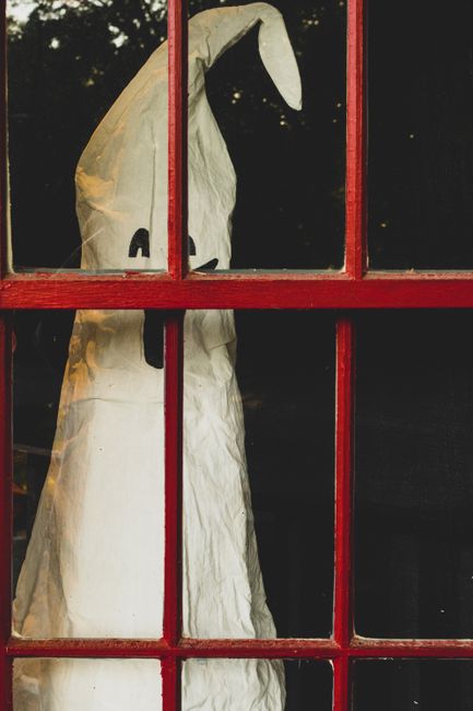 A ghost decoration seen through a red window frame, perfect for Halloween themes.
