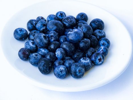 A close-up image of fresh, ripe blueberries piled on a white plate, highlighting their vibrant color and detail.