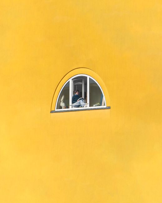 Person seen through arch window set in a vibrant yellow wall.