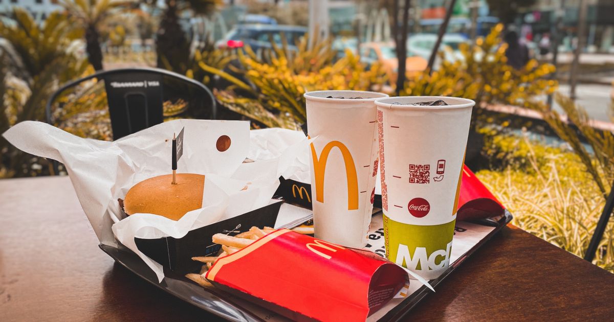 A fast food meal with a burger, fries and drinks on an outdoor table.