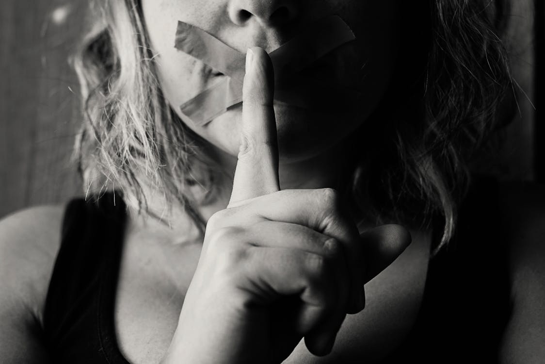 Woman Placing Her Finger Between Her Lips.  Her mouth is taped shut.