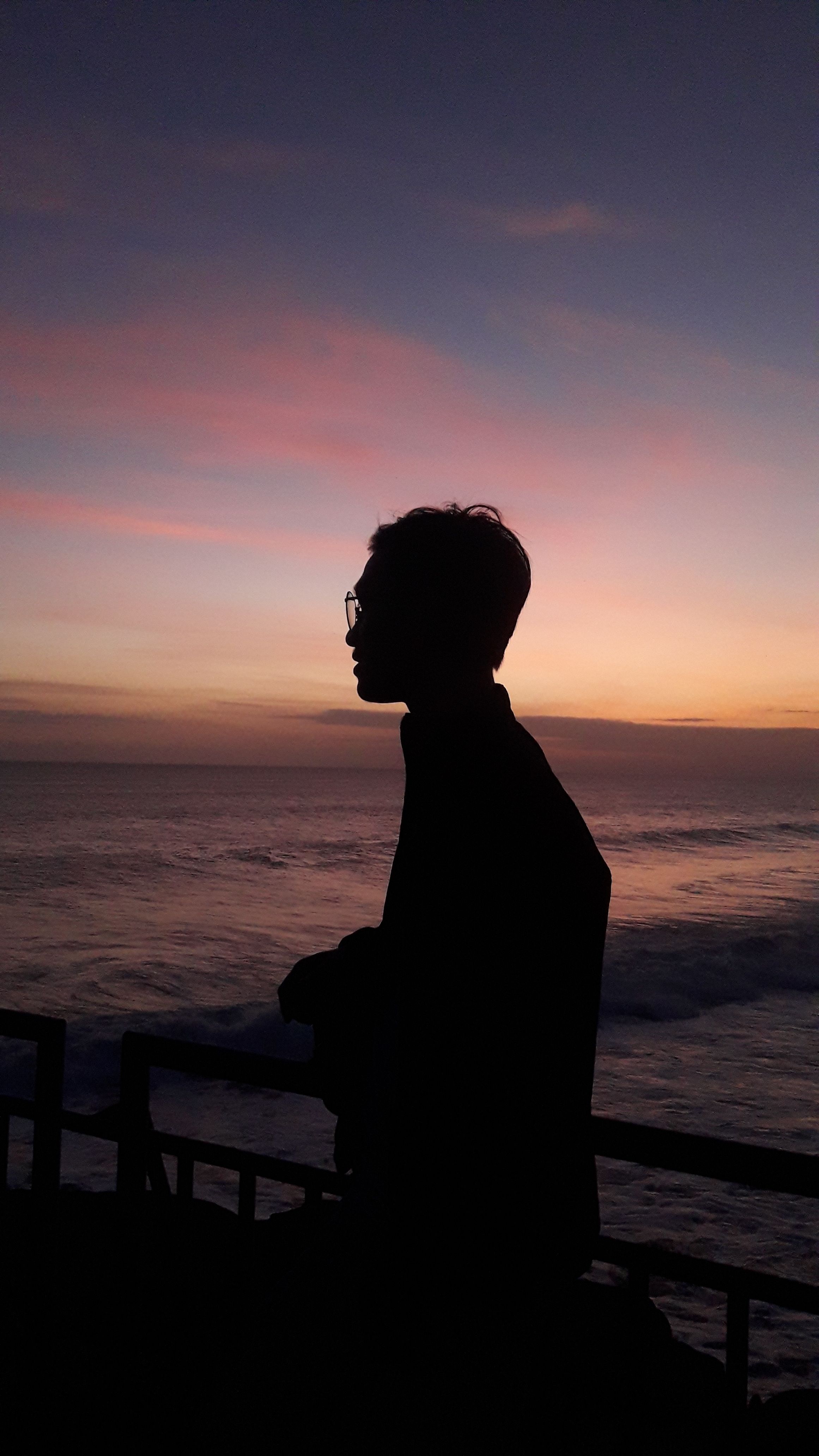 Silhouette of a person by the ocean during a vibrant sunset with colorful sky.