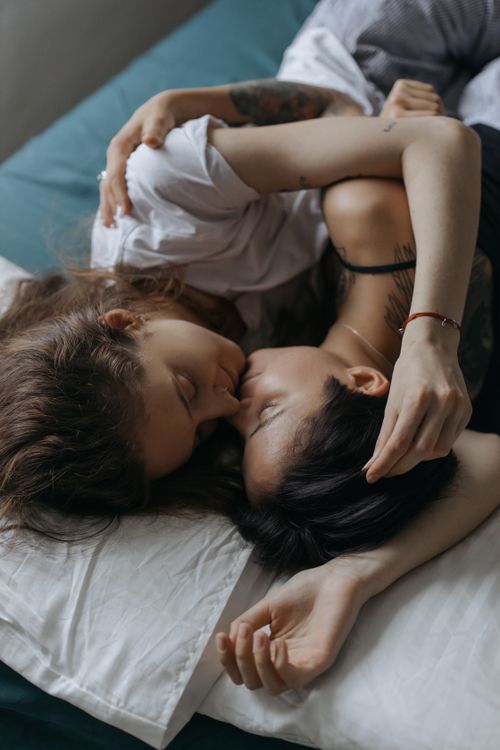 Free Two women sharing a close and romantic embrace, lying on a bed. Stock Photo