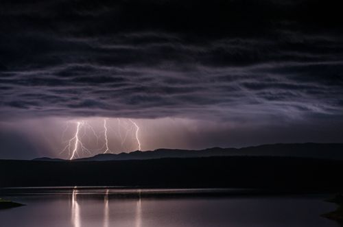 Free A dramatic thunderstorm with bright lightning strikes over a serene lake at night. Stock Photo