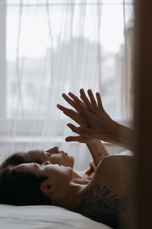 Free A romantic couple enjoying close moments while relaxing in bed, hands gently intertwined. Stock Photo