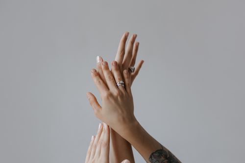 Free Minimalistic close-up of intertwined hands displaying rings, against a gray background. Stock Photo