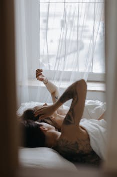 一对纹身的恩爱夫妇躺在床上，在柔和的自然光下享受着轻松的早晨