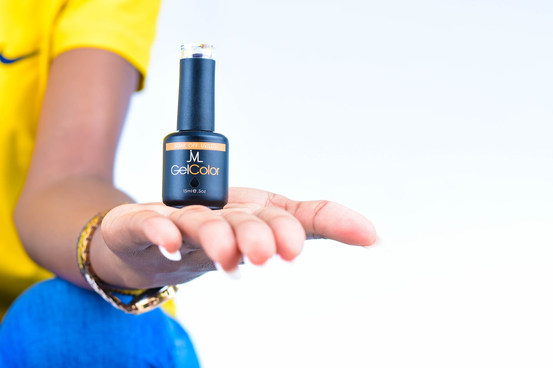 A woman's hand showcasing a gel nail polish bottle against a light background.