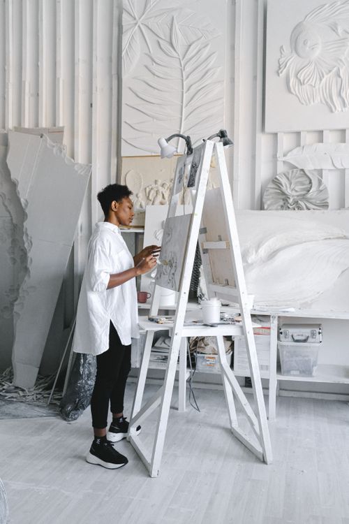 Free African American woman artist painting in a bright art studio surrounded by creative works. Stock Photo