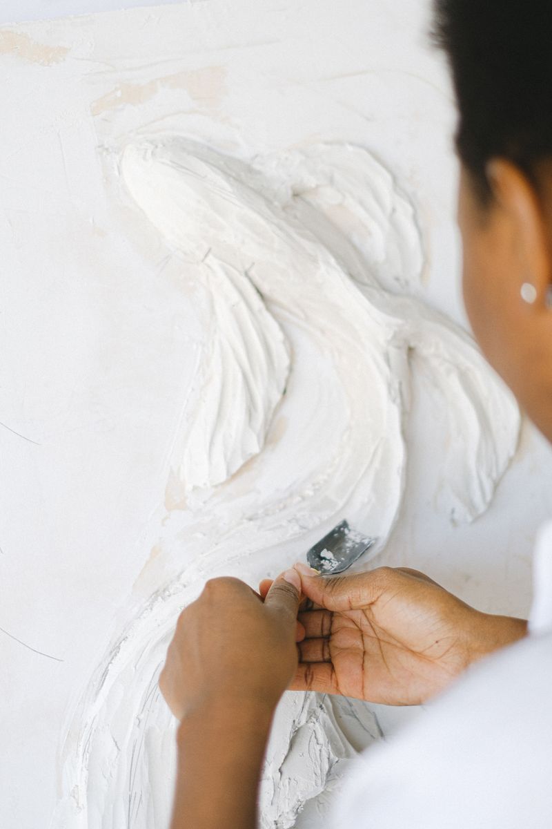 Close-up of a woman artist sculpting a fish design in plaster on a vertical surface