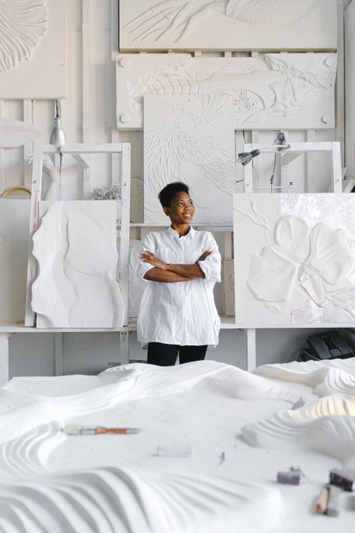 Free Artist standing in studio with abstract sculptures and paintings, arms crossed. Stock Photo