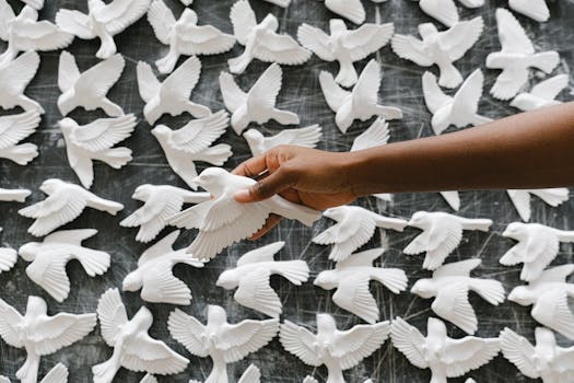 在多件类似艺术品的艺术展示中，一只手握着白鸟雕塑的特写