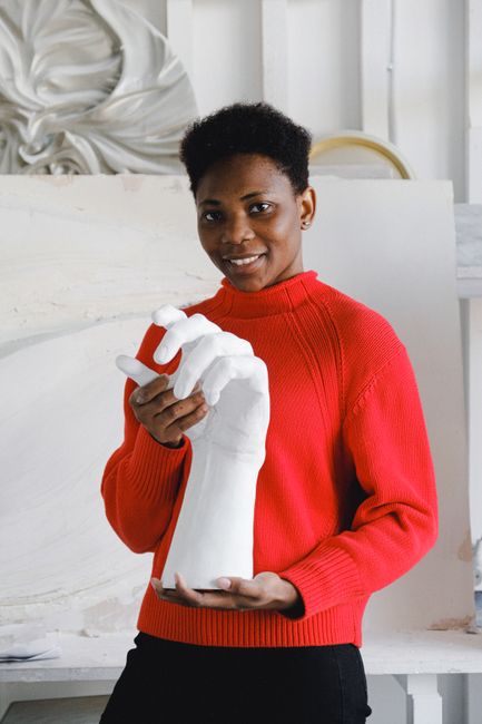 Portrait of a smiling artist in red sweater holding a white hand sculpture in an art studio.