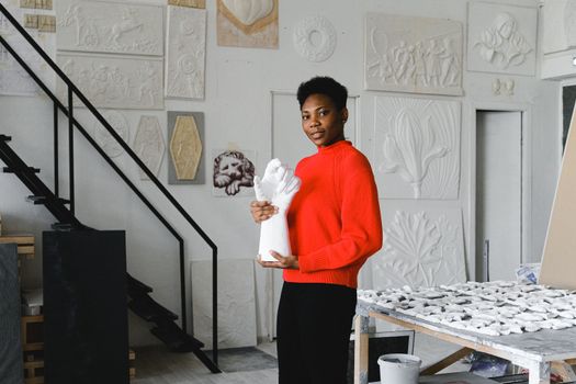 Artist holding ceramic piece in a bright workspace, showcasing craftsmanship and creativity.