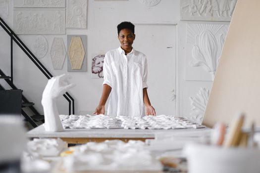 Woman in an art studio surrounded by sculptures and artworks, expressing creativity and focus.
