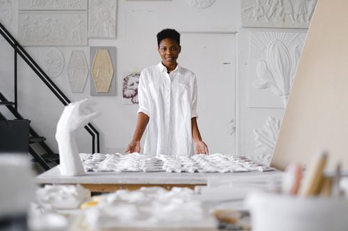 Free Woman in an art studio surrounded by sculptures and artworks, expressing creativity and focus. Stock Photo