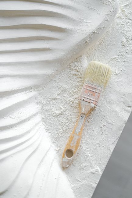 Detailed view of a paintbrush on a textured white plaster artwork surface.
